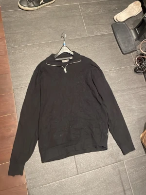 Svart halvzip tröja från Jack & Jones - Säljer en svart långärmad tröja från Jack & Jones med halvzip och hög krage. Tröjan är enkel och stilren, perfekt för lager på lager och funkar till det mesta. Materialet känns mjukt och bekvämt mot huden.