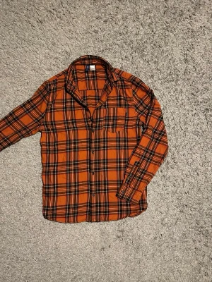 Rutig skjorta  - Säljer en riktigt schysst orange rutig skjorta. Skjortan har klassisk krage, bröstficka och knäppning framtill. Långärmad modell i mjukt bomullstyg, perfekt för dig som vill sticka ut med färg och mönster. 9/10 skick 🤩 Hör av dig om du har några frågor.