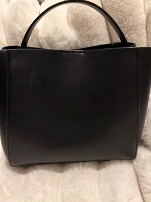 Svart väska från gina tricot  - Snygg väska från gina . Väskan har både ett kort handtag och en lång justerbar axelrem, perfekt för att bära crossbody. Enkel och modern look som passar till många outfits.