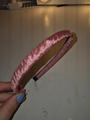 Rosa satin-diadem med twistad design - Säljer ett diadem i glansigt rosa satin med twistad och lindad design. Diademet har en mjuk struktur och är lätt att bära. Perfekt accessoar för att lyfta din look med en feminin touch.