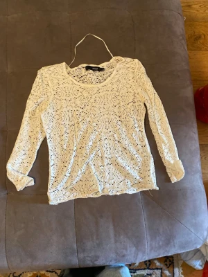 Vit spetsblus från Artist Clothing - Säljer en vit långärmad blus från Artist Clothing i genombruten spets med rund halsringning. Perfekt att styla med ett linne under för en trendig look. Blusen har fina spetsdetaljer och är lätt och luftig.