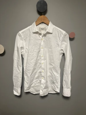 Vit slim fit skjorta från Replay - Klassisk vit skjorta från Replay i slim fit-modell. Skjortan har långa ärmar, knappar framtill och en liten broderad logga på bröstet. Tillverkad i bomull för en skön känsla och stilren look. Perfekt till jeans eller chinos.