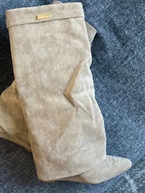 Boots - FRÅN LULIA!!Säljer ett par snygga beige stövlar i mjuk mocka med spetsig tå och bredare skaft. Stövlarna har en liten guldfärgad detalj upptill och en diskret klack. Perfekta för att lyfta din outfit med en trendig touch.