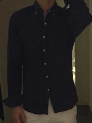 Mörkblå linneskjorta från John henric - Snygg mörkblå skjorta i linne med klassisk krage och vita knappar hela vägen framtill. Skjortan har lång ärm och en avslappnad passform, perfekt för en stilren look. Passar till både jeans och chinos.