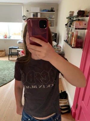 Grå AC/DC t-shirt med tryck - Cool grå t-shirt med stort AC/DC-tryck framtill och klassisk rund hals. T-shirten är kortärmad och har en avslappnad passform, perfekt för dig som gillar rock och vill ha en stilren bandtröja i garderoben.