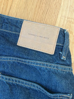 Blå raka jeans från H&M - Säljer ett par klassiska blå jeans från Hennes & Mauritz med raka ben och hög midja. Jeansen har två bakfickor och är sydda i slitstark denim med kontrastsömmar. Perfekta för en avslappnad och trendig look.