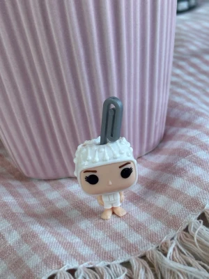 Stranger things eleven kinder joy Mini Funko Pop figur med ögla - Säljer en liten Stranger Things eleven kinder joy  Funko Pop-inspirerad figur med stort huvud, svarta ögon och vit outfit. Figuren har en grå ögla på huvudet, perfekt att hänga på väska eller nyckelknippa. Tillverkad i plast och har detaljerat ansikte och hår.