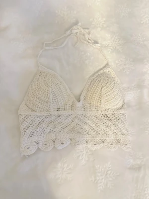 Vit virkad strand topp - Supersnygg vit virkad bikiniöverdel med halterneck och knyt i nacken. Toppen har vadderade kupor och dekorativ scallop-kant nedtill. Perfekt för stranden och ger en boho-vibe till din sommarstil.