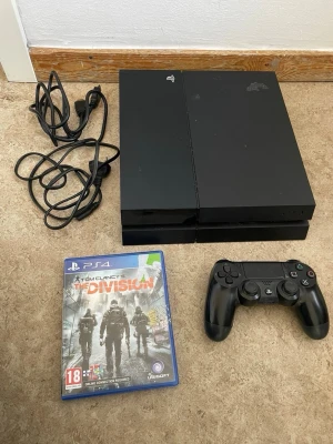 PlayStation 4 med handkontroll och spel - Säljer en svart PlayStation 4 med tillhörande svart DualShock 4-handkontroll, strömkabel och HDMI-kabel. Konsolen har en stilren, rektangulär design i plast. Spelet Tom Clancy's The Division till PS4 medföljer.