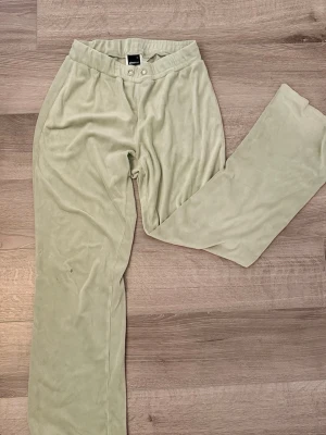 Ljusgröna mjukisbyxor Gina Tricot XS - Mysiga ljusgröna mjukisbyxor från Gina Tricot i mjukt velourmaterial. Byxorna har resår i midjan och två metallöljetter framtill för en cool detalj. Har små fläckar och några trådar är brutna (se bild 3 och 4)