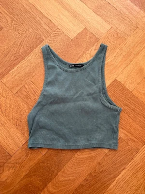Grön ribbad croppad linnetopp Zara - Säljer en grön ribbad croppad linnetopp från Zara. Toppen är ärmlös med breda axelband och har en enkel, stilren design. Perfekt att matcha med höga jeans eller kjol för en trendig look.