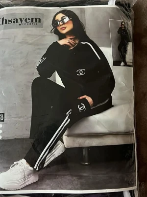 Svart loungewear set med vita detaljer - Snyggt svart loungewear set från Ahsayem Tekstil med vita ränder längs ärmar och ben. Setet har en oversized tröja och matchande byxor, båda med broderad logga framtill och på benet. Perfekt för chill dagar hemma eller när du vill vara bekväm men ändå se cool ut.