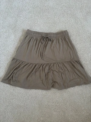 Ljusbrun volangkjol  - En jättefin ljusbrun kjol från Pieces i väldigt skönt material. Kjolen är i storlek XS och är helt ny med prislapp kvar.