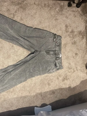 Grå tvättade raka jeans - Säljer ett par grå tvättade jeans med rak passform och klassisk femficksdesign. Jeansen har bälteshällor och knappgylf. Perfekta för en avslappnad och trendig look. Materialet är denim i bomull och färgen har en snygg tvättad effekt.