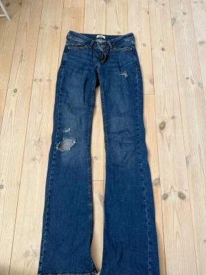 Blå bootcut jeans från ONLY - Säljer ett par blå lowwaist bootcut jeans från ONLY med slitna detaljer och hål på benet och på låret. Varan har tecken på användning se bild 4. 