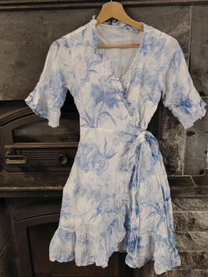 Studentklänning😍💎 Från LoveLolita! Nypris 120€ - Söt omlottklänning i vitt med ljusblått blommönster🌸🤍 Klänningen har korta puffärmar med volangkant, knytband i midjan och volang nertill. Materialet känns lätt och luftigt, perfekt för varma dagar☀️ Väldigt bra märke! Den har kostat 120€+posts💓 XS-M. 