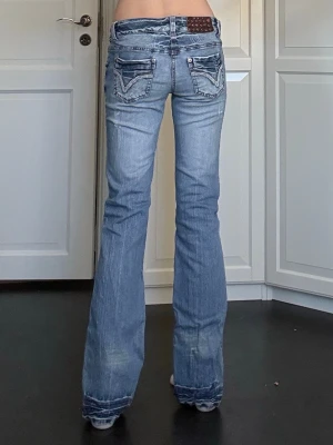 Blå bootcut jeans med låg midja - Snygga ljusblå bootcut jeans med låg midja och slitna detaljer. Jeansen har dekorativa bakfickor med kontrastsömmar och ”paljetter” på ettikett lappen. Endast använda 1 gång i min ägo, i bra skick. Midjemått är 37cm rakt över och innerbenslängden är 83cm. Vid frågor eller önskemål om fler bilder är det bara att skriva privat. 💕
