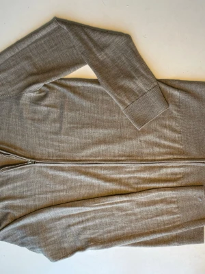 Beige ziptröja från H&M - Snygg beige ziptröja från H&M i mjukt stickat material. Tröjan har hög krage, hel dragkedja framtill och ribbade muddar vid ärmslut och nederkant. Perfekt för lager på lager och enkel att matcha med olika outfits.