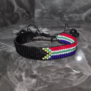 Sydafrikanska flaggan Handgjort armband - ✨️Justerbart, enkelt att öppna och stänga ✨️Kan stängas till en 15cm omkrets och öppnas bredast till ca 27cm omkrets ✨️Höjden av flagg-delen är 1,3cm ✨️Flagg-delen minus knuten är 14cm lång ✨️Skickas inom en vecka så fort tillverkningen är klar