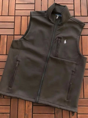 Helt ny Polo Ralph Lauren Väst Svart (Stl M) - Snygg svart väst från Polo Ralph Lauren med dragkedja framtill och tre praktiska fickor med dragkedja. Västen har en stilren look med det klassiska Polo-logotypen broderad på bröstet. Perfekt att slänga över en hoodie eller tröja för extra stilpoäng.