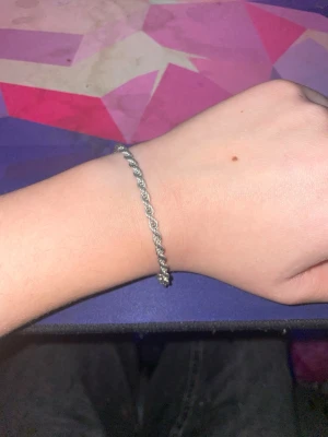 Flätat silverfärgat armband - Snyggt armband i silverfärg med flätad design. Passar perfekt för dig som gillar stilrena accessoarer med en twist. Lätt att matcha med andra smycken och har ett klassiskt spänne.