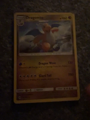 Dragonite Pokémonkort - Dragonite Pokémonkort med gul ram och färgglad illustration av Dragonite mot en molnig bakgrund. Kortet har 160 HP och attacker som Dragon Wave och Giant Tail. Baksidan har klassisk blå design med Pokéball och Pokémon-logga.