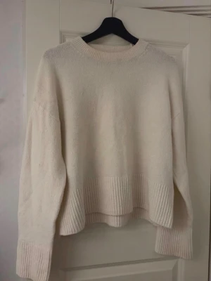 Vit stickad tröja - Mysig stickad tröja i offwhite med breda ribbade muddar vid ärmslut och nederkant. Tröjan har rund halsringning och avslappnad passform. Några fläckar på tröjan och missfärgad runt halsen, ej tvättad så kan försvinna.