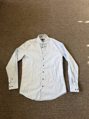 Ljusblå slim fit skjorta i bomull - Snygg ljusblå skjorta från dressman i slim fit-modell. Tillverkad i mjuk bomull med paisleymönstrad insida på kragen. Långärmad med knappar framtill och vid ärmslut. Perfekt för en clean och stilren look.