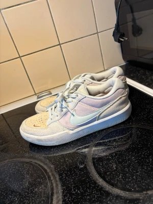 Nike SB Force 58 pastell sneakers - Nike SB Force 58 sneakers i pastellfärger med beige mocka framtill, ljusblå swoosh och detaljer i ljuslila. Skorna har vita snören och en vit sula. Perfekta för dig som gillar streetwear och skate-inspirerad stil. Storlek 40, innermått 25cm.