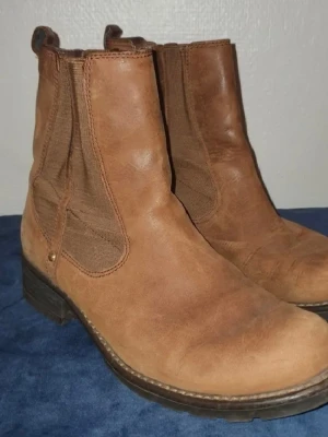 Bruna Chelsea boots i skinn - Snygga bruna Chelsea boots i äkta skinn med elastiska paneler på sidorna och robust sula. Klassisk rund tå och dragflikar upptill för enkel påtagning. Perfekta för dig som vill ha en stilren och tidlös look till hösten. Storlek 38