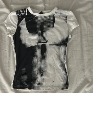 Vit och svart grafisk t-shirt - Cool t-shirt med ett svartvitt grafiskt tryck framtill som skapar en edgy look. T-shirten är kortärmad och har en figurnära passform. Perfekt för dig som vill sticka ut med en unik och konstnärlig stil.