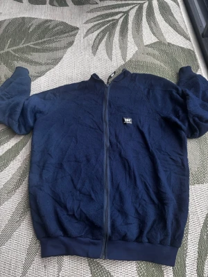 Mörkblå fleecejacka Helly Hansen - Mysig mörkblå fleecejacka från Helly Hansen med dragkedja framtill och liten logga på bröstet. Jackan har ribbade muddar vid ärmslut och nederkant samt hög krage. Perfekt för lager-på-lager och chill dagar. Pris kan diskuteras 