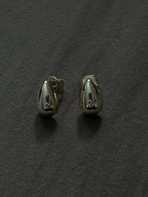 Droppformade silvriga örhängen - Snygga örhängen i droppformad design med blank, silvrig yta. De har en stilren och modern look och är perfekta för dig som gillar minimalistiska accessoarer. Örhängena har klassisk stiftbaksida och är tillverkade i metall.