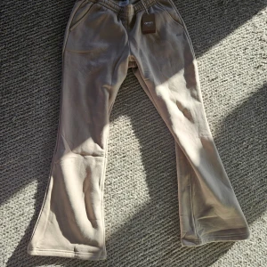 Beige mjukisbyxor från Aimn - Säljer ett par helt nya  beige mjukisbyxor från Aimn med utsvängda ben och resår i midjan. Byxorna har dragsko och sidofickor, tillverkade i mjukt bomullsmaterial. Perfekta för en avslappnad och trendig look.