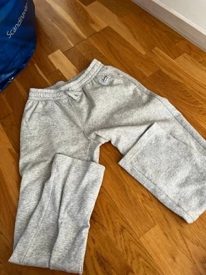 Grå mjukisbyxor från Andy by Frank Dandy - Snygga grå mjukisbyxor från Andy by Frank Dandy med resår och dragsko i midjan. Byxorna har raka ben och är tillverkade i mjukt sweatshirtmaterial. Perfekta för chill eller träning, med enkel och clean design. Fickor på sidan av byxan, ej på baksidan.