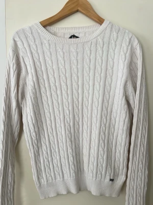 Vit kabelstickad tröja  - Kabelstickad vit tröja från  blanc du nil med rund halsringning och långa ärmar. Tröjan har ribbade muddar vid ärmslut och nederkant samt en liten metallbricka med logga nertill. Köpt från blanc du nil i Frankrike för några månader sen för 36 EUR