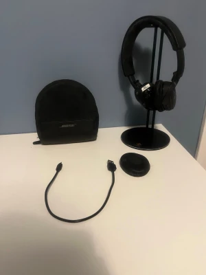 Bose hörlurar och hörlurställ  - Bose On-Ear trådlösa hörlurar i svart (produktkod SLOEBK). Slitna och en lossnad öronkudde går lätt att fixa hos reparatör. Hörlurställ i perfekt skick. Tar gärna prisförslag.