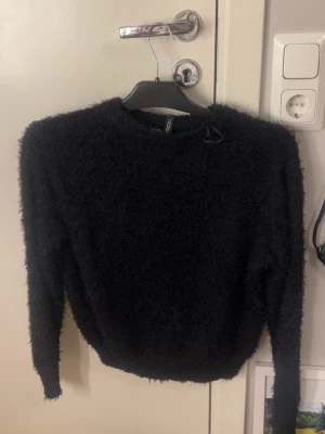 Svart fluffig stickad tröja H&M Divided - Mysig svart stickad tröja från H&M Divided i fluffigt material. Tröjan har rund halsringning, långa ärmar och ribbade muddar. Perfekt för kalla dagar när du vill vara både bekväm och snygg!