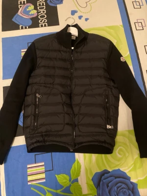 Svart cardigan från Moncler - Snygg svart cardigan från Moncler med quiltad front och ärmar i stickad ull. Jackan har dragkedja framtill, två sidofickor med dragkedja och en liten Moncler-logga på ärmen. Perfekt för dig som vill ha en stilren och bekväm jacka. Passar för 13-14 år i storlek 160-170cm, om mått behövs är det bara skriva! Väldigt ny använts några gånger.