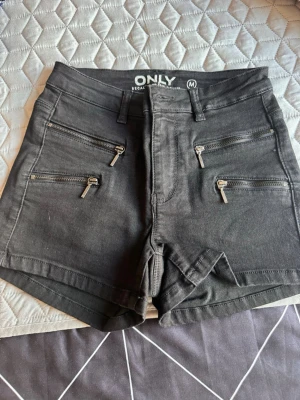 Svarta jeansshorts från ONLY - Snygga svarta jeansshorts från ONLY med fyra dragkedjefickor fram och två bakfickor. Modellen är kort och har bälteshällor i midjan. Materialet är stretchigt denim som sitter bekvämt och följer kroppen.