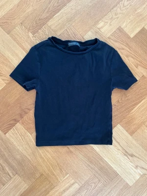 Svart basic t-shirt från Stradivarius - En enkel svart t-shirt från Stradivarius med rund hals och korta ärmar. Tillverkad i mjuk bomull för en bekväm känsla. Passformen är normal och modellen är klassisk utan några extra detaljer eller mönster.