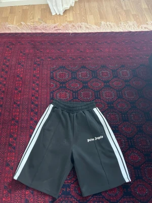 Palm Angels svarta skorts med vita ränder - Palm Angels skorts i svart med vita sidoränder och elastisk midja. Klassisk sportig look med logotypen tryckt på vänster ben. Tillverkade i ett mjukt, stretchigt material som ger en avslappnad och trendig vibe. Pris kan diskuteras vid snabb och smidig affär😊😊