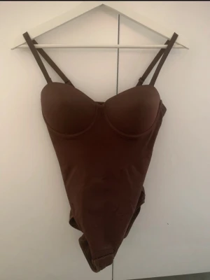 3-pack bodys  - Säljer tre bodys med bygel och vadderade kupor, en i brunt, svart och en i beige. 