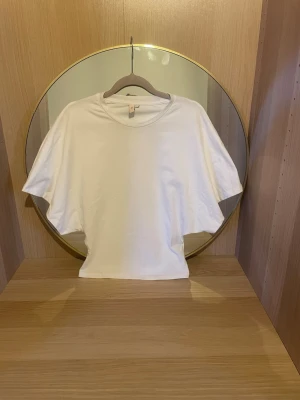 Vit t-shirt från Nelly - Klassisk vit t-shirt från Nelly i mjuk bomull. Modellen har rund halsringning och korta ärmar med en relaxed passform. Perfekt basplagg att styla till olika outfits.sitter tajt vid midjan och löst vis ärmarna. Pris kan diskuteras!💗helt ny och aldrig använd men prislappen är tyvärr bortklippt💕