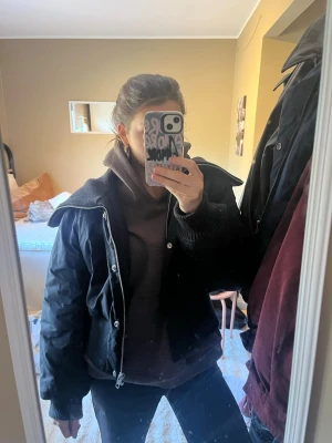 Svart pufferjacka från Weekday - Säljer en svart pufferjacka från Weekday med dragkedja och knappar framtill. Jackan har en bred krage och är tillverkad i ett quiltat material som håller värmen.