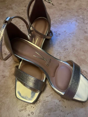 Metallic sandaler med blockklack - Snygga metallicfärgade sandaler från Vagabond med fyrkantig tå, bred rem över foten och justerbar ankelrem med spänne. Blockklack ger stabilitet och komfort. Tillverkade i skimrande syntetmaterial med mjuk innersula för extra bekvämlighet.