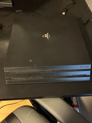 Sony PlayStation 4 Pro konsol svart - Säljer en svart PlayStation 4 Pro från Sony. Konsolen har en stilren, fyrkantig design med tre lager och PlayStation-loggan i silver på ovansidan. Materialet är matt plast och färgen är helsvart. Perfekt för gaming och streaming.