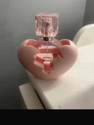 Ariana Grande rosa parfymflaska - Snygg parfym från Ariana Grande i en rosa flaska med hjärtformad hållare. Perfekt för dig som vill ha en trendig och unik accessoar på sminkbordet. Volym och ingredienser syns ej på bilderna.
