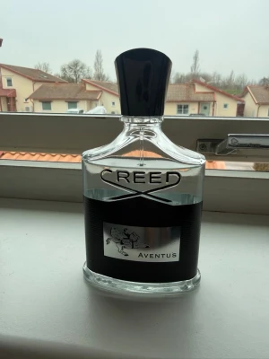 Creed Aventus parfym 100ml - Exklusiv parfym från Creed, modellen Aventus. Flaskan är genomskinlig med svart etikett och silverdetaljer, samt en svart plastkork. Klassisk och lyxig design som passar perfekt för dig som gillar eleganta dofter.