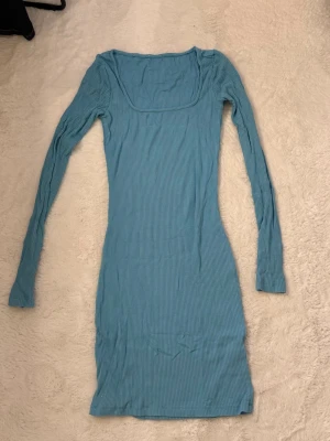 Ljusblå ribbad långärmad klänning - Tight, ljusblå ribbad klänning med lång ärm och fyrkantig ringning. Klänningen är kort och har en kroppsnära passform som framhäver siluetten. Perfekt för dig som gillar enkel men stilren design.